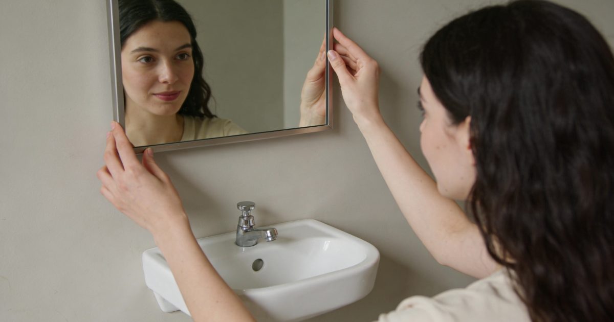 Femme ajuste miroir mural au dessus petit lavabo